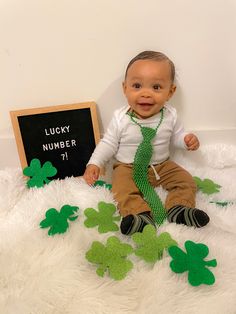 a baby wearing a green tie sitting next to shamrocks