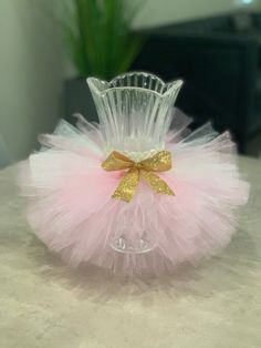 a glass vase with a pink tutule and gold bow on the top sitting on a table