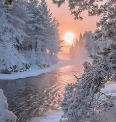 the sun is setting over a river surrounded by snow covered trees