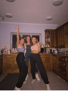 three women standing in a kitchen posing for the camera with their arms up and hands raised