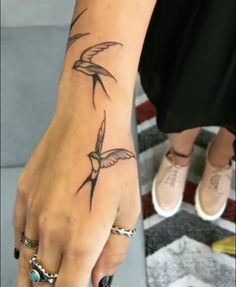 a woman's hand with a bird tattoo on her left wrist and two rings