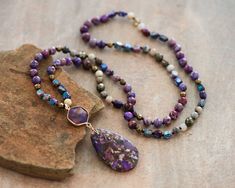 "Approx. 34\" L. Pendant size: 1.2\"x3\" Color, size, pattern may vary. Elevate your style with our enchanting Purple Sea Sediment Imperial Jasper Necklace, featuring a substantial stone pendant for a bold and distinctive look. Meticulously handcrafted, this necklace is not just a stunning accessory but also a symbol of stability and healing. The large Purple Sea Sediment Imperial Jasper pendant takes center stage, displaying a mesmerizing blend of deep purples and rich blues. Known for its stabilizing energy, this gemstone promotes a sense of calm and balance. The necklace goes beyond mere fashion, offering a connection to the earth's energies and a shield of healing crystal protection. Measuring approximately 34 inches, the knotted design showcases the natural beauty of Purple Sea Sedime Bohemian Crystal Pendant Necklace With Faceted Beads, Purple Agate Bohemian Beaded Necklaces, Spiritual Purple Agate Beaded Necklaces, Purple Agate Spiritual Beaded Necklace, Bohemian Purple Beaded Necklaces With Polished Beads, Bohemian Faceted Beads, Gems, And Cabochons For Gifts, Handmade Purple Agate Beaded Necklaces, Bohemian Faceted Beads For Gifts, Crystal Beaded Necklace