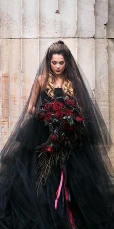 a woman wearing a black wedding gown with red flowers