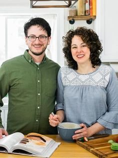 a man and woman standing next to each other at a kitchen counter with a bowl of food in front of them