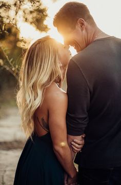 a man and woman standing next to each other with the sun shining through trees behind them