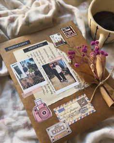 a coffee cup and some papers on a bed next to a vase with purple flowers