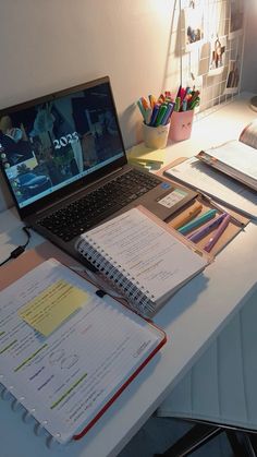 an open laptop computer sitting on top of a desk next to a pile of books