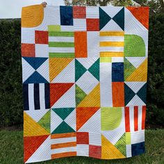 a colorful quilt hanging on the side of a wooden pole in front of some bushes