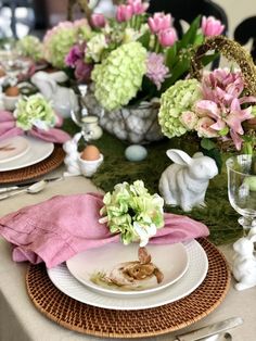 the table is set with pink and green flowers in vases, plates and napkins