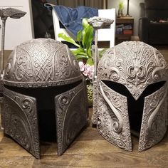 two silver helmets sitting on top of a wooden table next to a vase with flowers