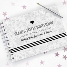 a white notebook with pink stars on it and a black heart in the middle is next to a pen that says blue's 50th birthday