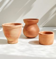 three clay pots sitting next to each other on a white tableclothed surface with shadows from the wall behind them