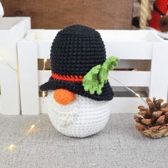 a crocheted snowman hat next to a pine cone on a white bench