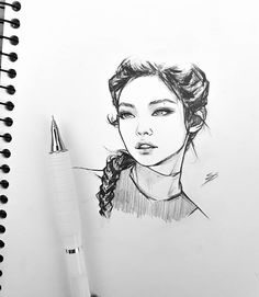 a pencil drawing of a woman's face on a notepad next to a pen