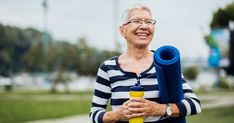 an older woman holding a blue yoga mat and a yellow water bottle