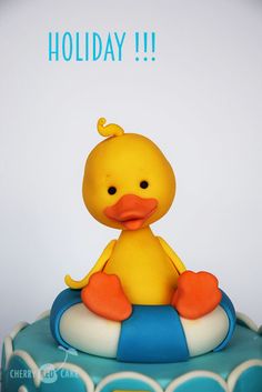 a yellow rubber ducky sitting on top of a blue and white cake with the words holiday written above it