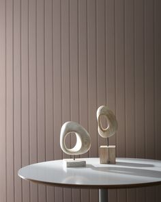 two sculptures sitting on top of a white table next to a brown wall with vertical stripes