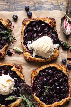 four blueberry pies with ice cream on top and some sprigs next to them