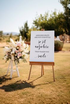 a sign with flowers on it sitting in the grass next to an easel that says,