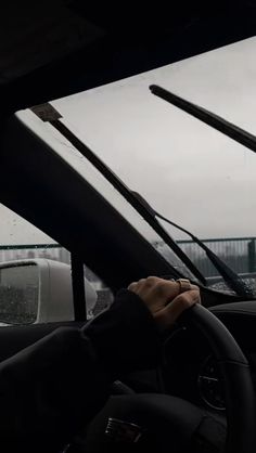 a person driving a car in the rain with their hands on the steering wheel and windshield