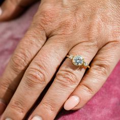 a woman's hand with an engagement ring on her left and the middle finger