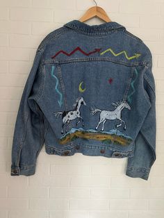 This jacket is not just any denim jacket--it's a rare vintage find! Made by the retro brand Jordache, it screams classic style and quality craftsmanship. What makes it truly special is its stunning hand-painted design featuring majestic horses and a Western theme. With its size XL, it offers a comfortable and relaxed fit. Whether you're a collector of vintage clothing or simply appreciate timeless pieces with a touch of artistry, this jacket is sure to turn heads and elevate any outfit.  Measurement Info Across the Shoulders is approx. 21.5 inches Shoulder to Cuff approx. 25 inches Neck to Hem 30 inches Pit to Pit approx. 21 inches  Please message me If you need any other details about this item. Vintage Denim Jacket With Graphic Print For Spring, Vintage Graphic Print Denim Jacket For Spring, Artsy Long Sleeve Denim Jacket For Fall, Artsy Denim Jacket For Fall, Hand Painted Long Sleeve Denim Jacket For Fall, Artistic Hand Painted Denim Jacket For Fall, Horses Western, Male Shirt, Majestic Horses