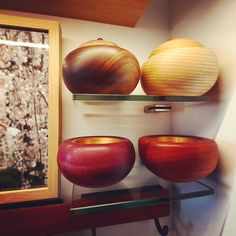 three wooden bowls are sitting on shelves in front of a window and another bowl is next to it