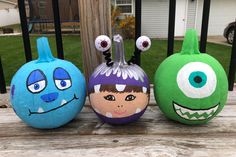 three painted pumpkins sitting on top of a wooden table