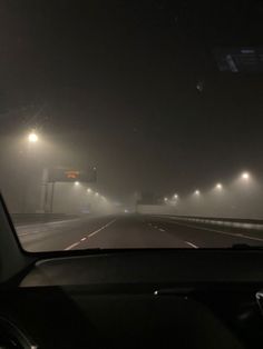 the view from inside a car driving on a foggy road at night with street lights