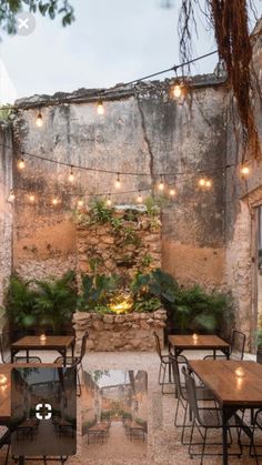 an outdoor dining area with tables, chairs and lights strung from the stone wall above