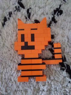 an orange and black cat made out of legos on a white rug, with one piece missing