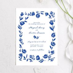 a blue and white wedding card with flowers on the front, surrounded by greenery