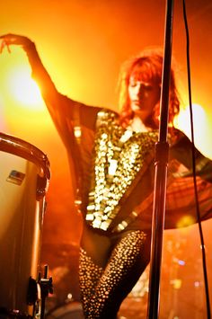 a woman standing next to a microphone on top of a stage with her arm in the air