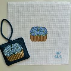 a cross - stitch card with a blue flowered cupcake on it and an embroidered ornament hanging from the front