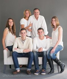 a group of people sitting on top of a white couch in front of a gray wall