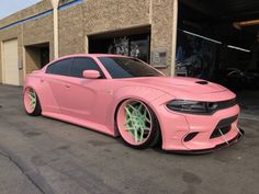 a pink car parked in front of a building with green wheels and rims on it