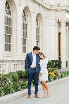 a man and woman standing next to each other on the sidewalk in front of a building