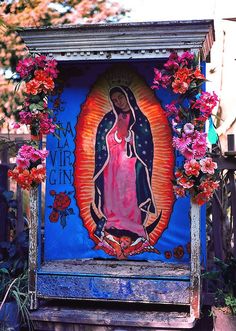 an image of the virgin mary on display in a shrine surrounded by flowers and greenery