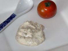 a tomato sitting on top of a white plate next to a spoon