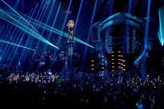 the singer is standing on top of a pole in front of an audience