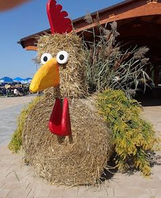 a fake chicken made out of hay sitting on top of a sidewalk