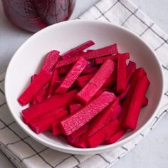 a white bowl filled with beets on top of a table next to a jar of liquid