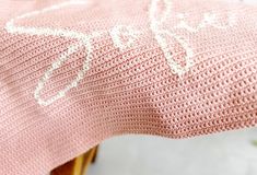 a pink knitted blanket sitting on top of a wooden chair next to a plant