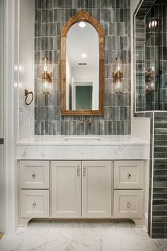 a bathroom with marble counter tops and white cabinets, along with a gold framed mirror