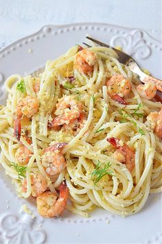 a white plate topped with pasta and shrimp next to a silver serving fork on top of a table