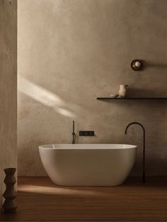 a white bath tub sitting on top of a wooden floor next to a wall mounted faucet