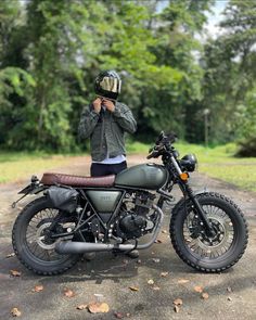 a man standing next to a motorcycle on a dirt road with trees in the background