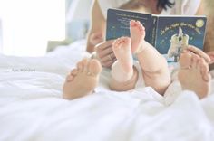 a woman reading a book to her baby on the bed with their feet propped up