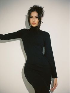 a woman posing in a black dress with her arms behind her head and hands on her hips