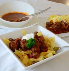 two square plates filled with pasta and meatballs next to a bowl of tomato soup